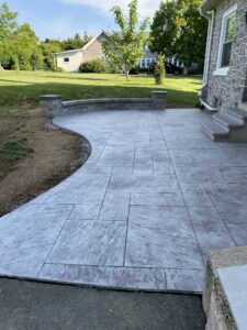 Decorative stamped concrete patio installation with a modern slate pattern and curved stone retaining wall by Morrison Custom Concrete."