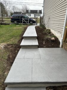 Newly installed decorative concrete sidewalk with integrated steps, featuring a light gray stamped finish for a clean, modern look."