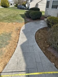 Curved stamped concrete walkway with textured stone pattern leading to front entrance of suburban home