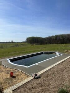 Freshly poured smooth concrete pool deck installation around in-ground swimming pool with scenic open field view